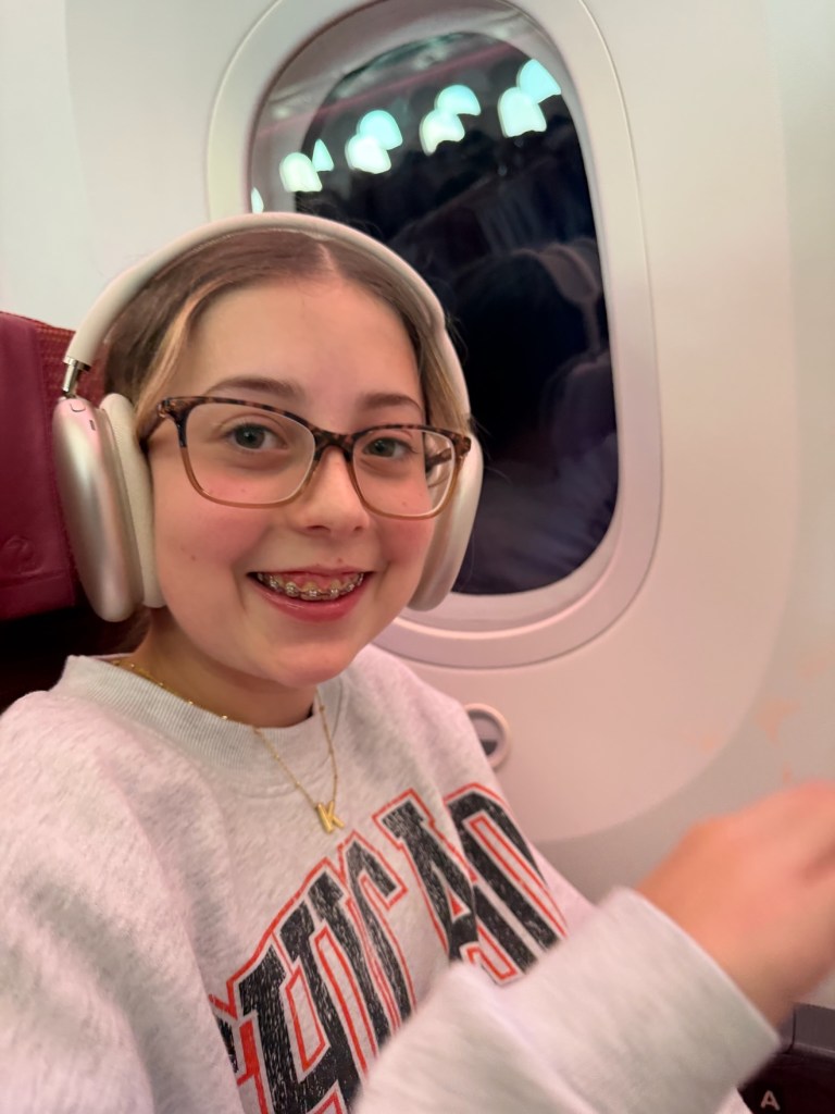 Kennedy wearing glasses and white over-ear headphones in her airplane window seat