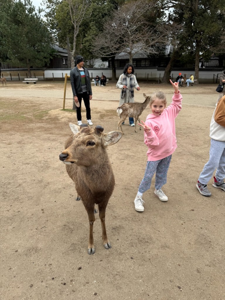 Sawyer in a pink hoodie flashing a peace sign next to a deer
