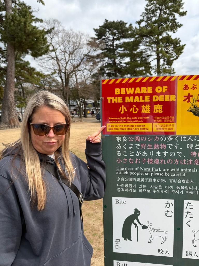 Devon pointing at a Beware of the male deer warning sign in Nara Park